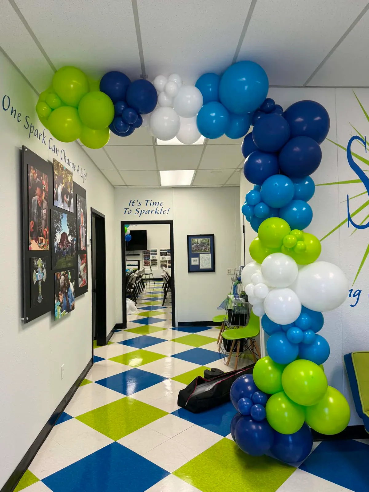 Navy, blue, lime-green, and white balloon garland arching over a hallway doorway beside a wall reading One Spark Can Change A Life
